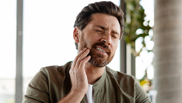 Man grimacing and holding jaw, suggesting tooth or jaw pain