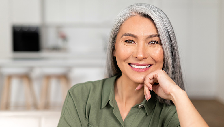 Smiling woman with gray hair resting chin on hand in a bright home setting