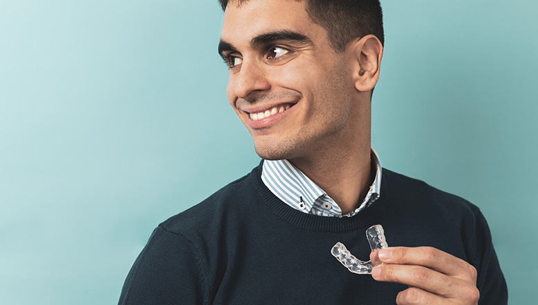 Smiling man holding clear dental aligner against blue background